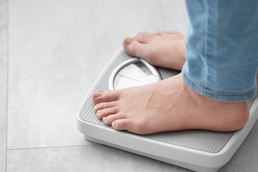 Young woman standing on scales at home, closeup. Weight loss concept.