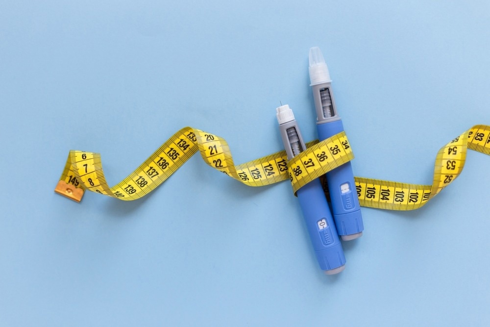 Two injectors dosing pens for subcutaneous injection of antidiabetic medication or anti-obesity medication hovering over a blue background. Yellow measuring tape around the injectors.