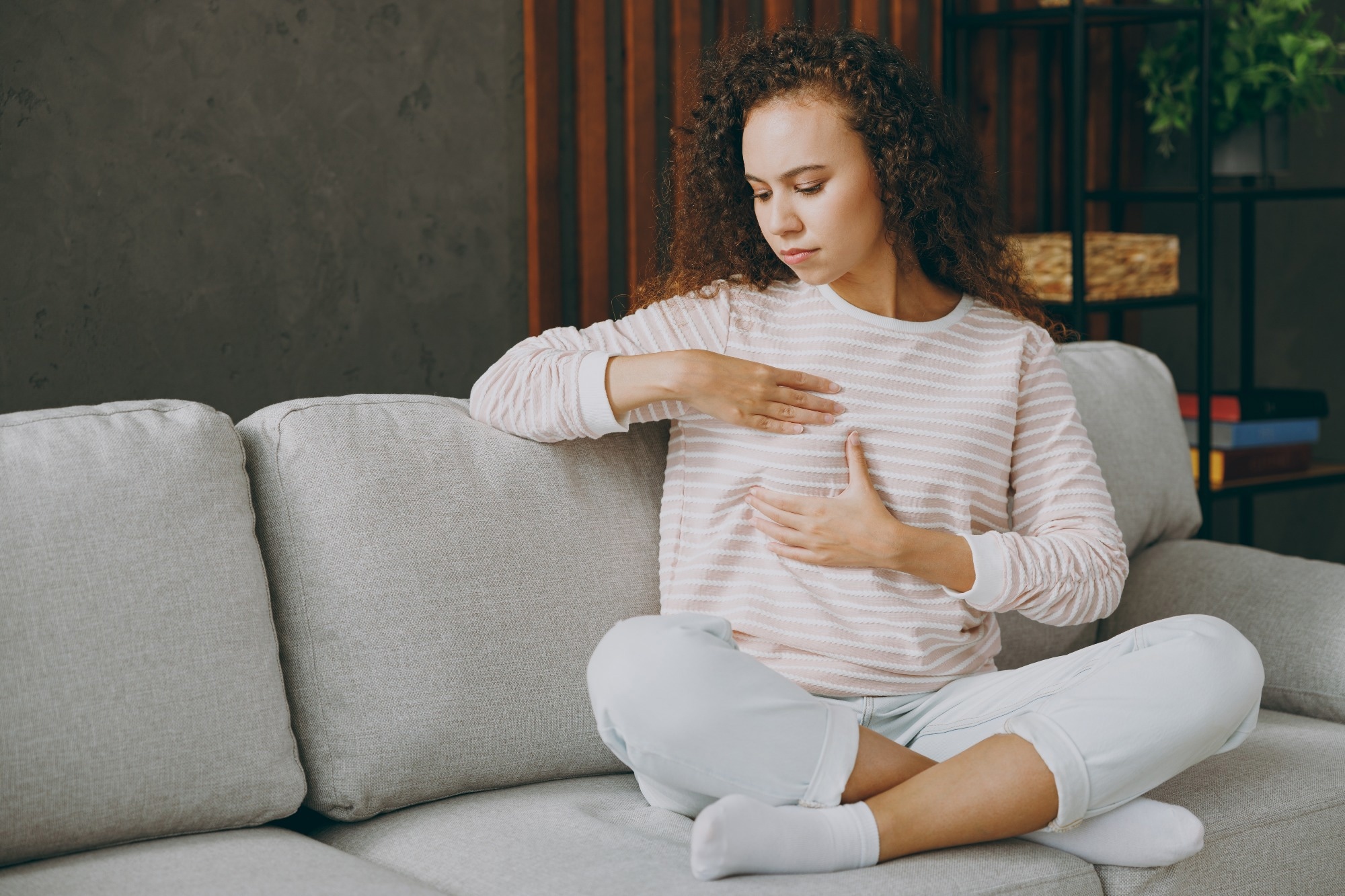 Full body young woman wearing casual clothes sits on grey sofa couch hold touch breast check health.