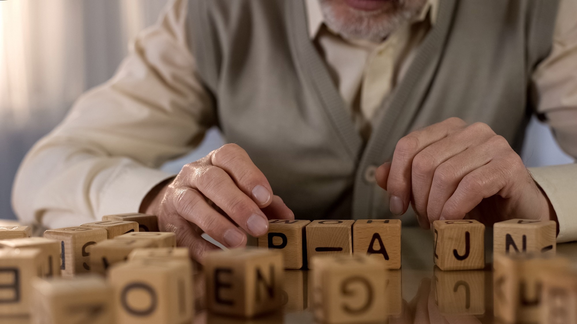 Male pensioner trying to make word of wooden cubes.