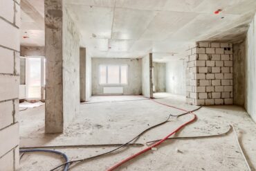 Built structure construction site of residential apartment building. Interior in progress to new house with windows and white brick wall with electric colored wires on the floor.