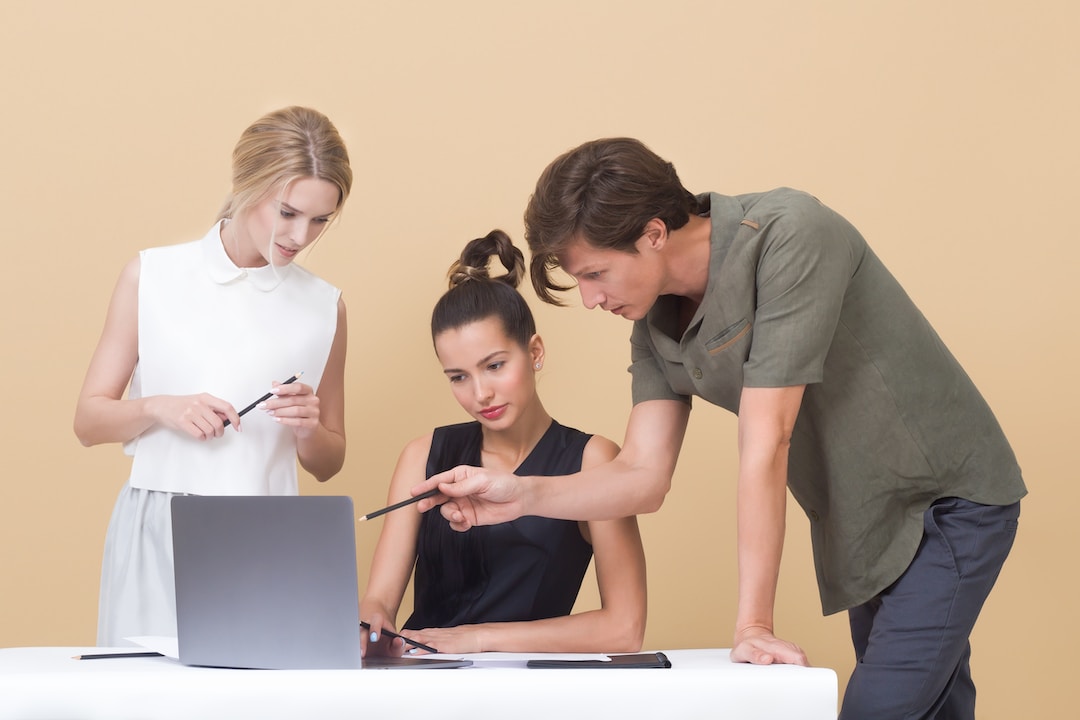 Three people against a tan background looking at a laptop screen discussing proposal automation.